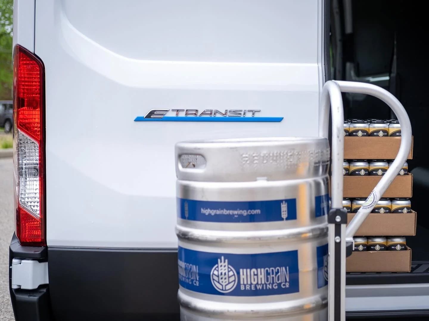 The back of a white Ford Transit van with a highgrain keg and boxes of cans in the cargo area.