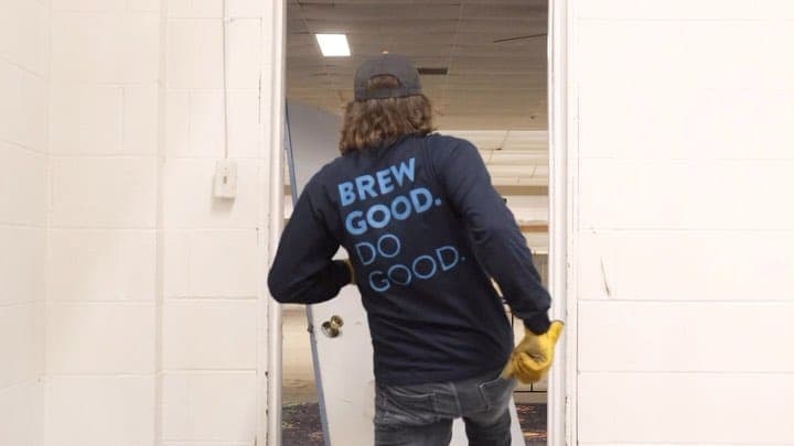 A HighGrain team member in a Brew Good Do Good hoodie opening the door to the old Brentwood Bowl