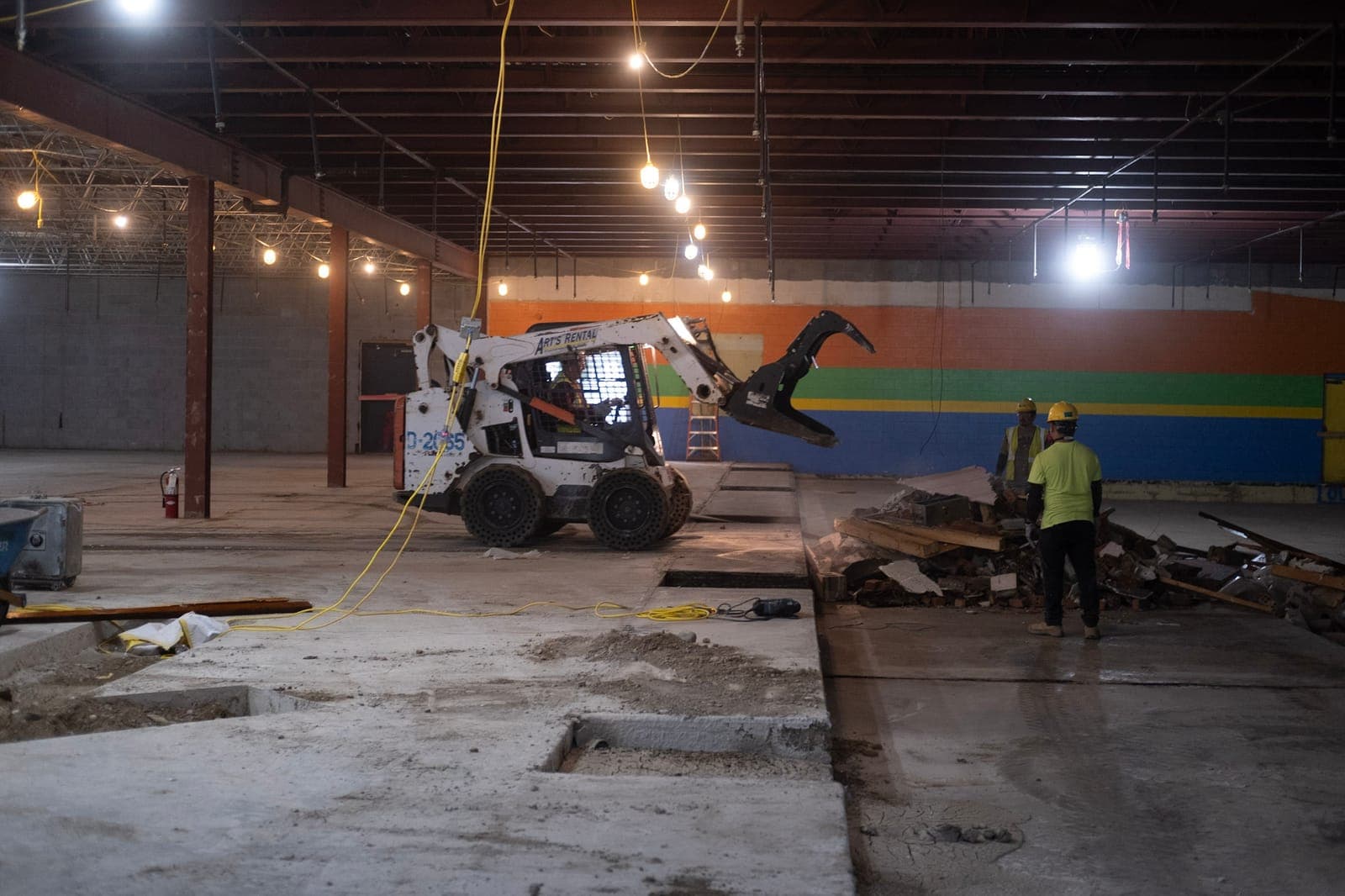 A skid steer clearing debris inside the former Brentwood Bowl, its rainbow wall still in place