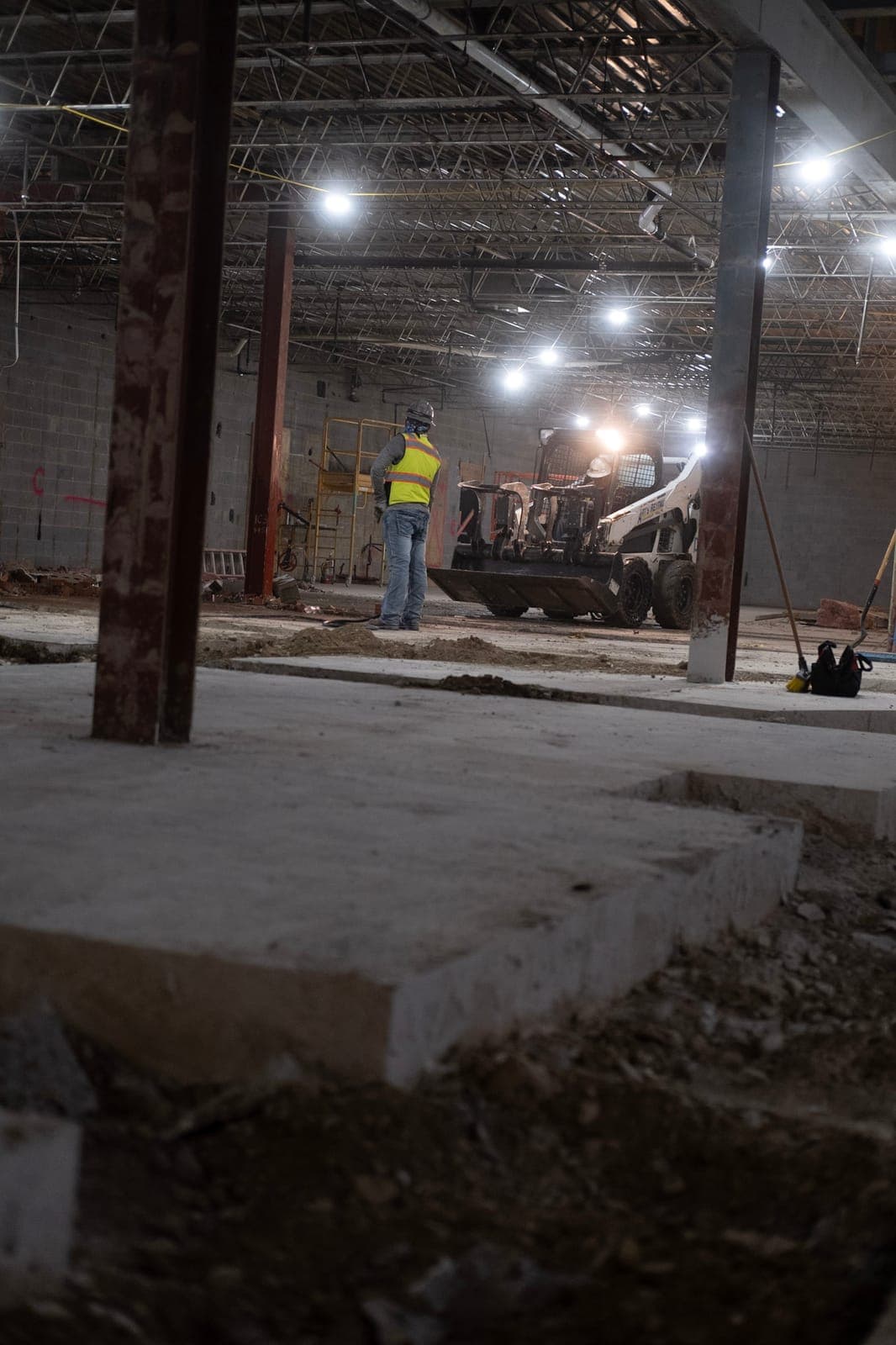 A worker in a safety vest beside a skid steer during interior demolition