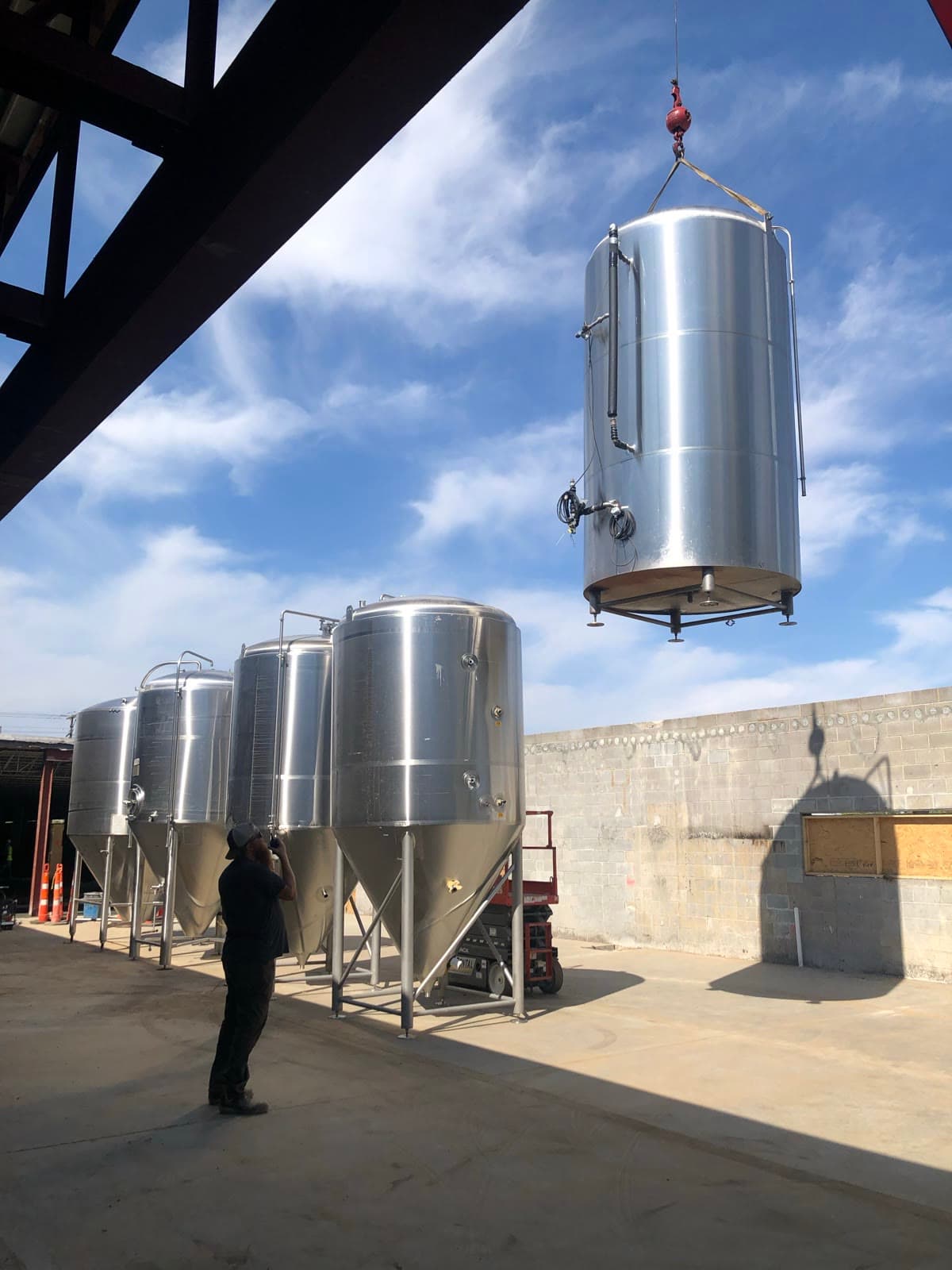A crane lowers a fermentation tank beside a row of fermenters at the Brentwood brewery