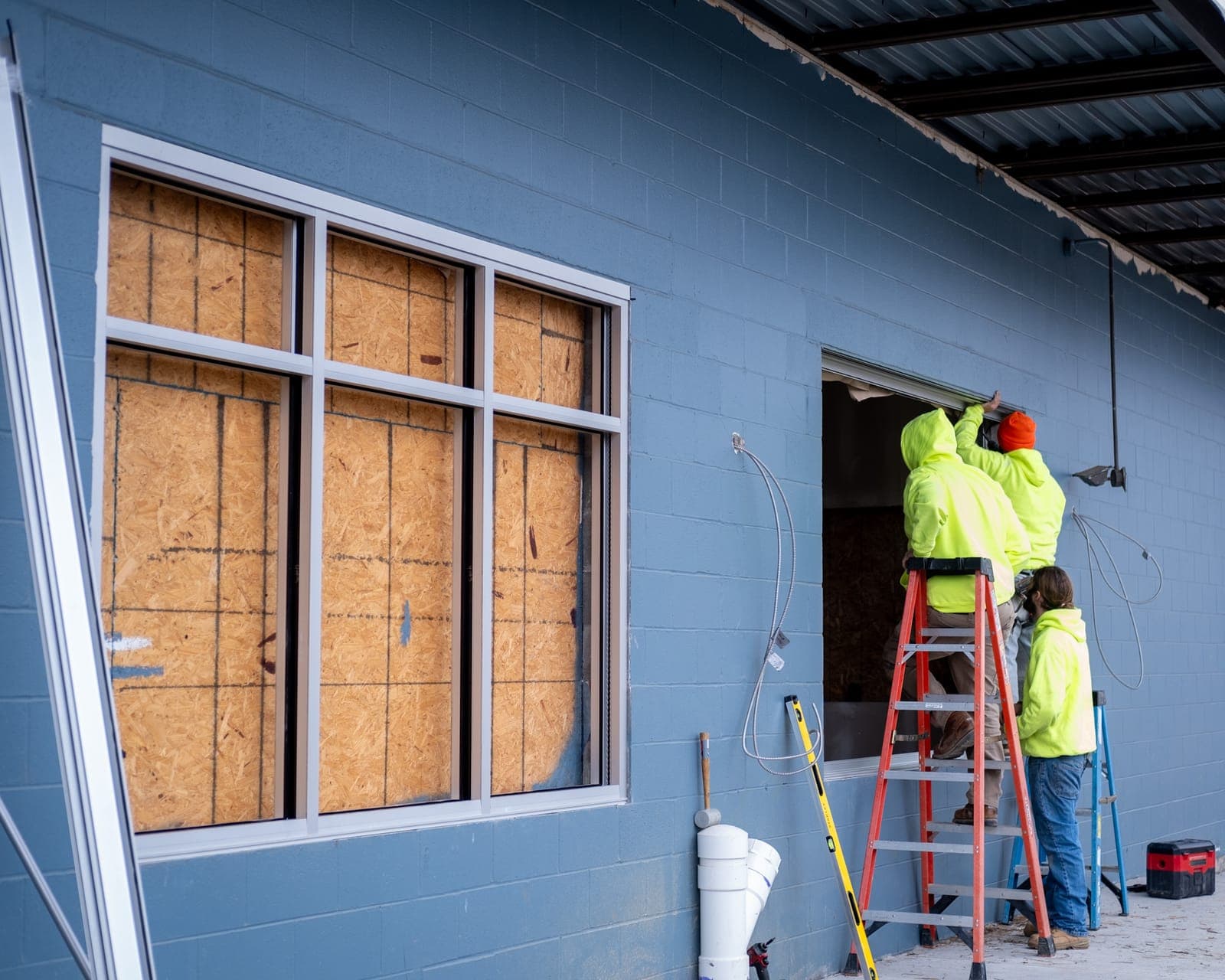 A worker on a ladder installing windows on the blue exterior