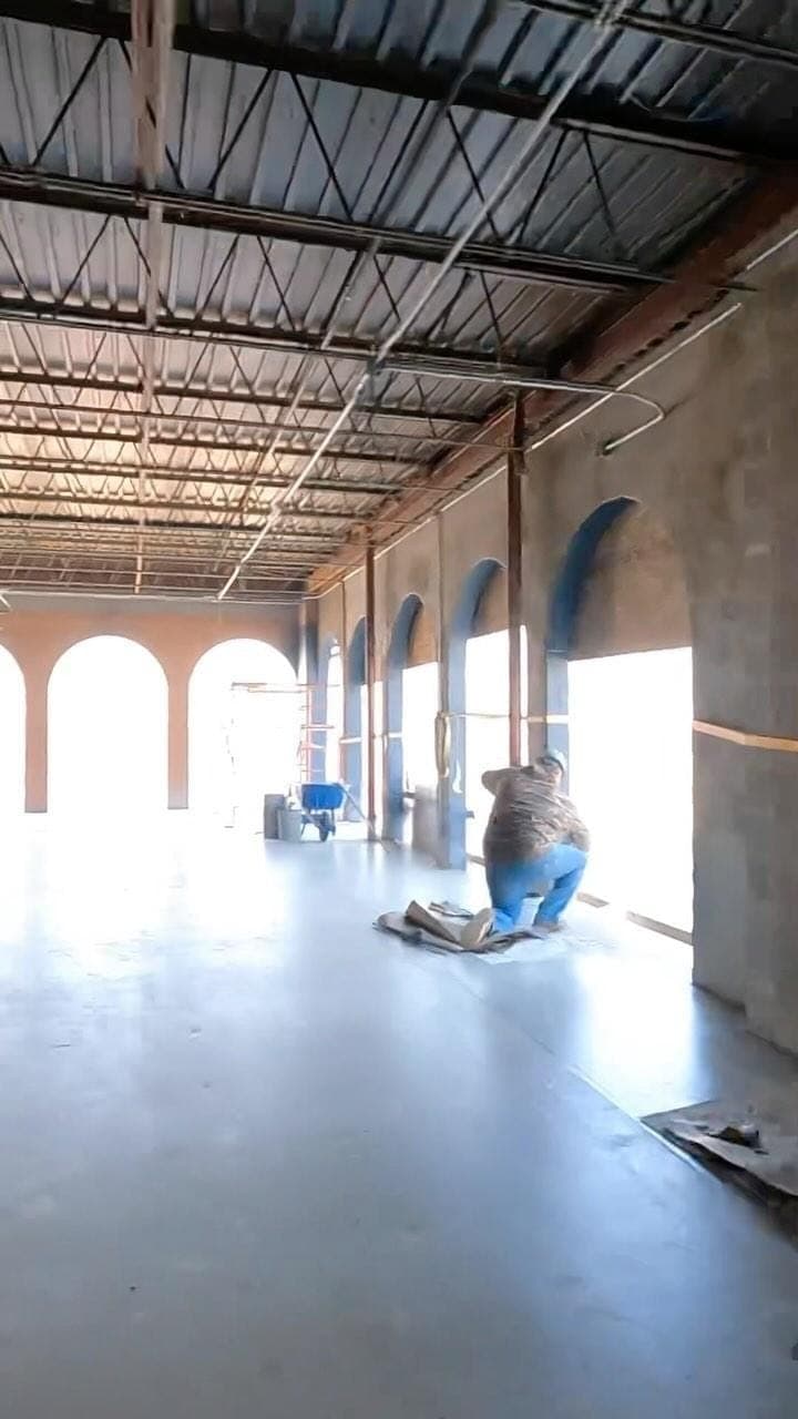 A worker finishing the floor beneath the arched windows
