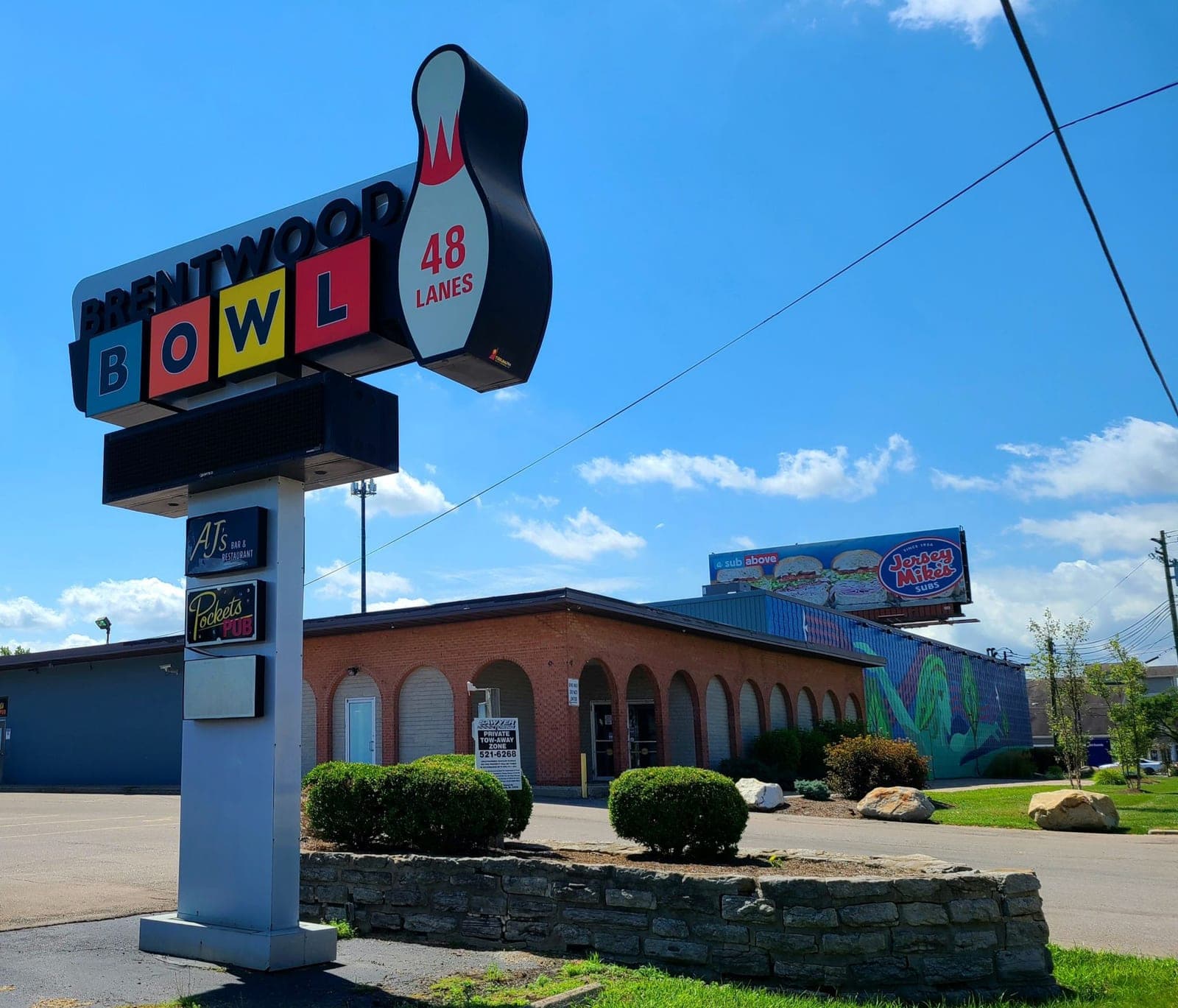 The Brentwood Bowl sign, 48 lanes, in front of the arched brick building and its mural before construction