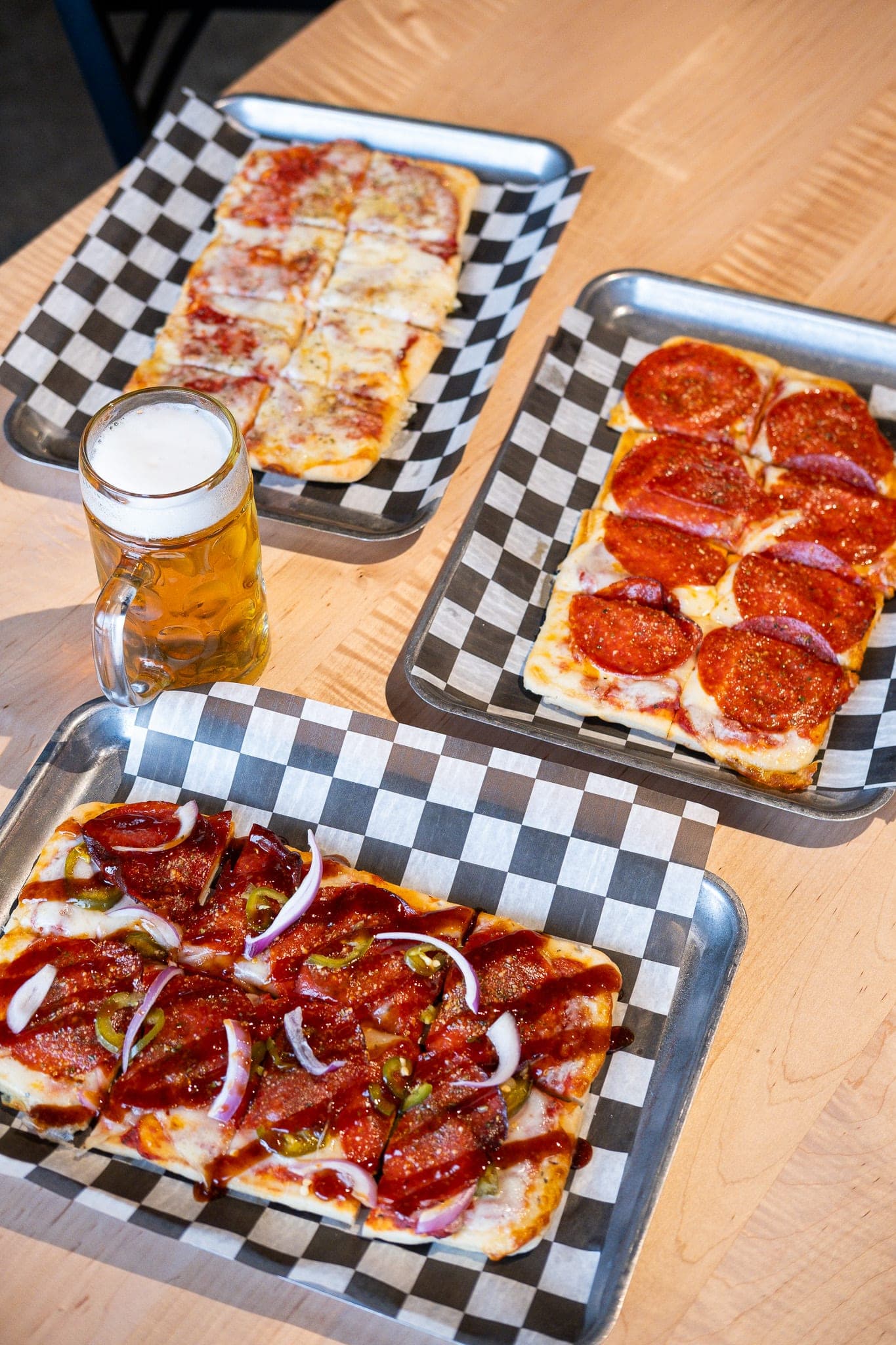 Three flatbread pizzas on checkered trays with a beer