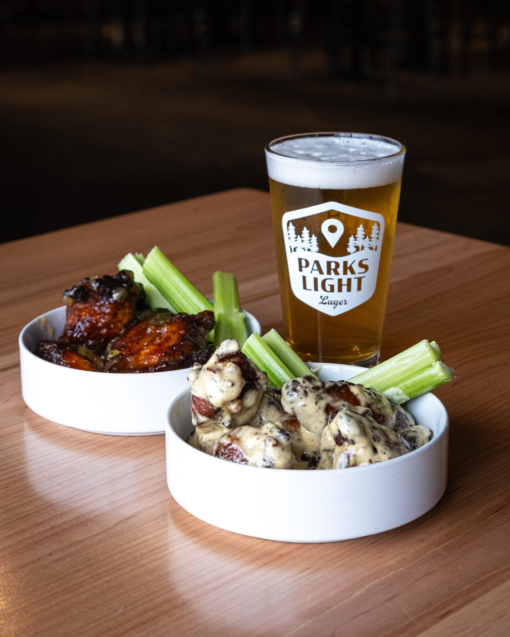 Two bowls of wings with celery next to a Parks Light pint