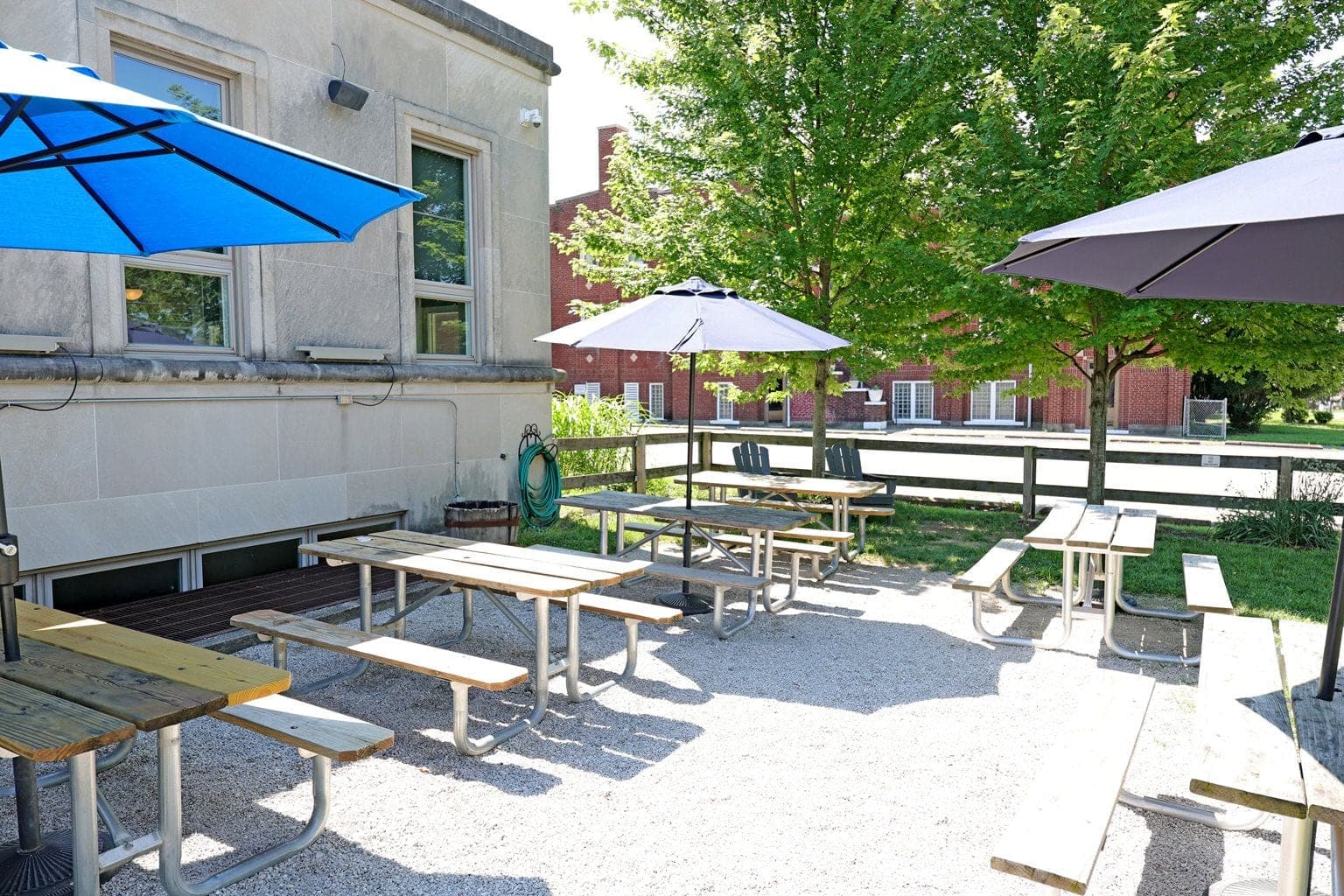 Picnic tables and umbrellas in the gravel beer garden under shade trees